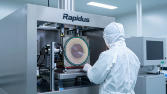 Cleanroom technician beside semiconductor wafer-processing equipment at an advanced chip factory.