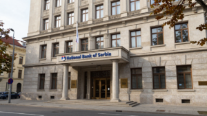 National Bank of Serbia headquarters in Belgrade with a Serbian flag nearby.