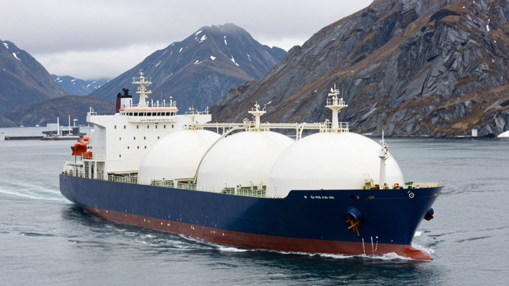LNG carrier sailing near an Alaskan coast with mountains and an export terminal in the distance.