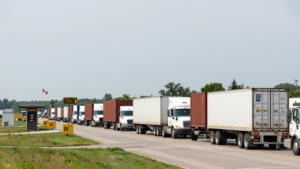 Freight trucks and shipping containers queue at a Canada–U.S. border crossing.