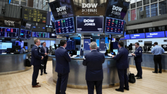 Traders on the New York Stock Exchange floor beneath screens displaying rising U.S. stock indexes.
