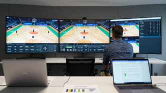 Coach reviewing sports footage and analytics on screens in a video-analysis room.