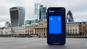 Smartphone with a digital banking app set against London’s Canary Wharf financial district.
