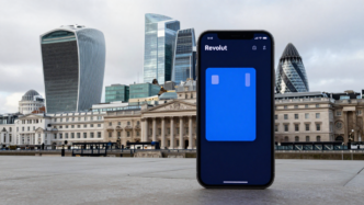 Smartphone with a digital banking app set against London’s Canary Wharf financial district.