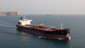 Oil tanker transiting the Strait of Hormuz with another vessel and Middle Eastern coastline in the distance.