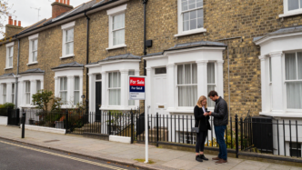 A couple considers a terraced house for sale on a British residential street.