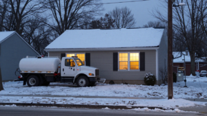 Northeastern home with a heating-oil tank and delivery truck on a winter evening.
