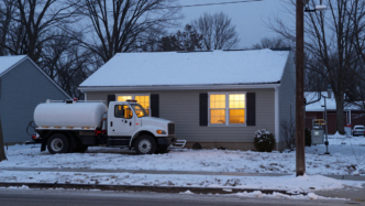 Northeastern home with a heating-oil tank and delivery truck on a winter evening.