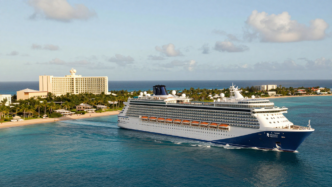 Royal Caribbean cruise ship sailing near a Caribbean beachfront resort.