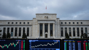 The Federal Reserve building in Washington, D.C., with financial-market graphics in the foreground.
